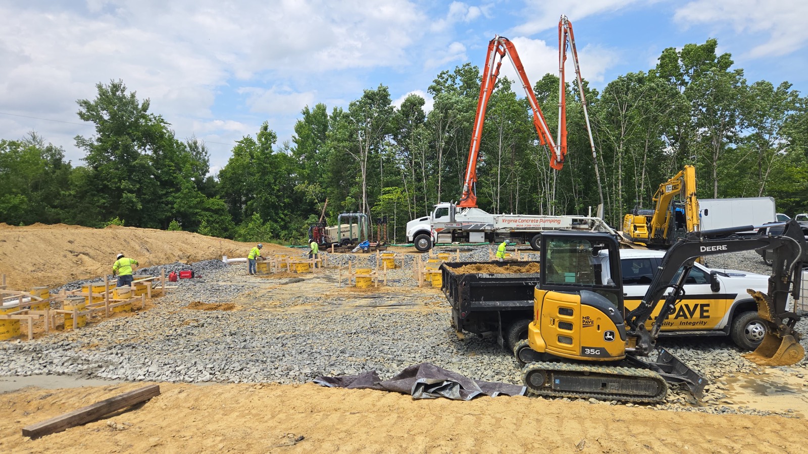 Excavator and dump truck positioned beside footing forms on an active site, part of drainage tie-in work