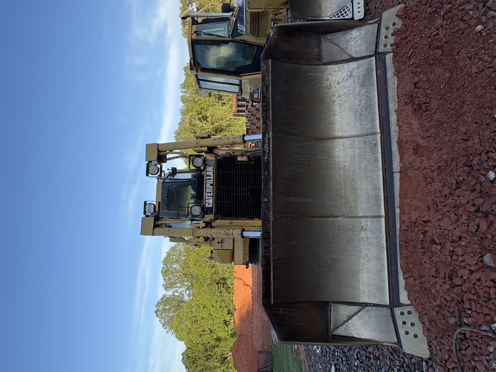 CAT loader bucket positioned over gravel and graded soil on a construction site