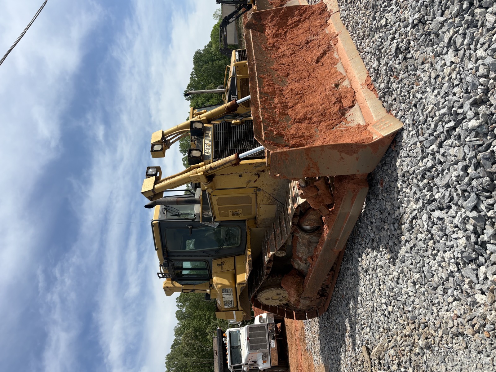 CAT loader placing a bucket of graded red-clay soil next to a gravel base course